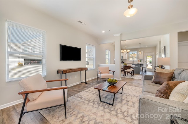 living area featuring visible vents, baseboards, recessed lighting, an inviting chandelier, and wood finished floors