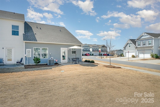 rear view of house featuring a residential view, central AC unit, a shingled roof, and a patio