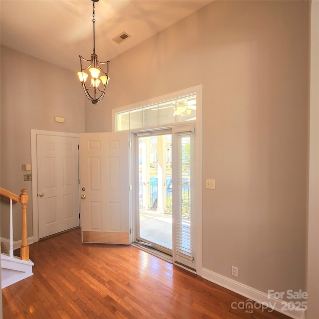 foyer featuring stairway, wood finished floors, visible vents, baseboards, and an inviting chandelier