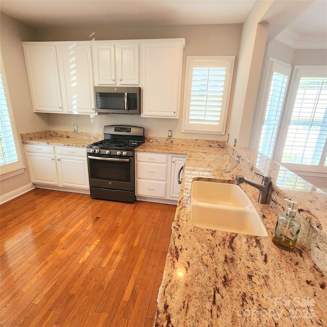 kitchen with a sink, stainless steel appliances, white cabinets, and light wood finished floors