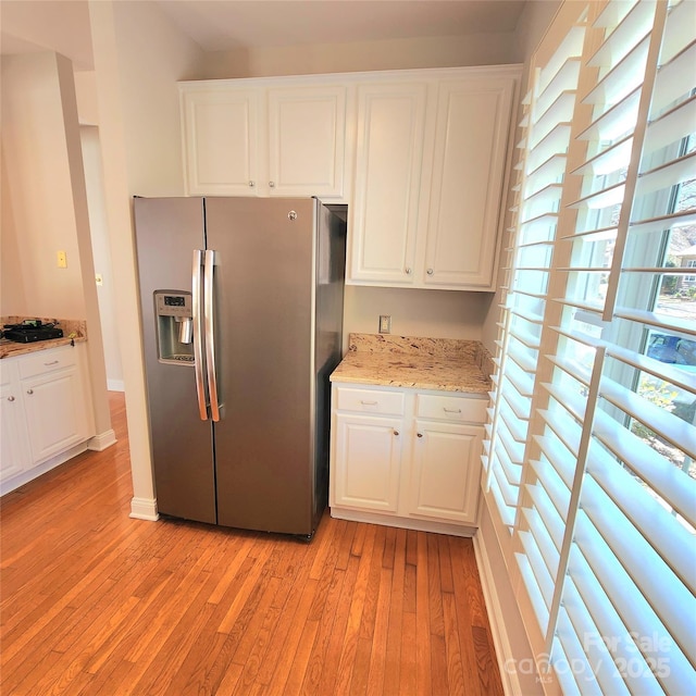 kitchen with light stone counters, baseboards, light wood-style flooring, white cabinets, and stainless steel fridge