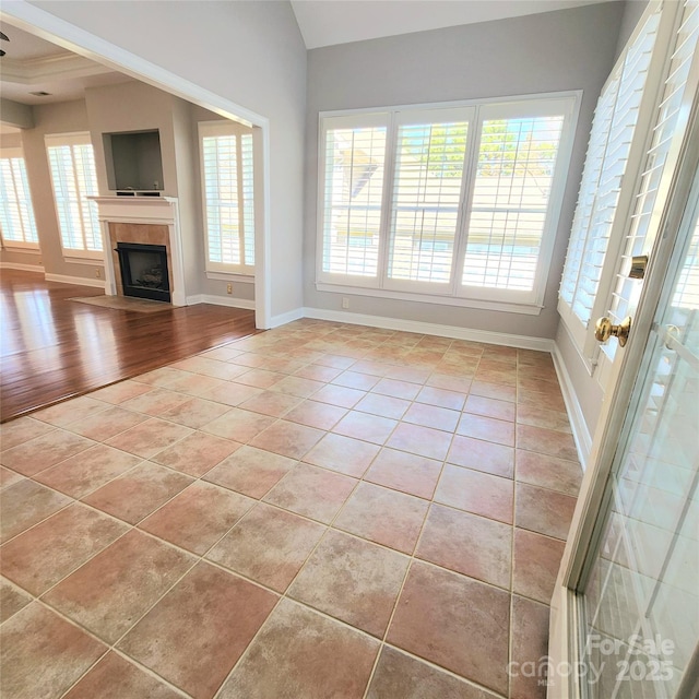 unfurnished living room featuring a tiled fireplace, vaulted ceiling, light tile patterned floors, and baseboards