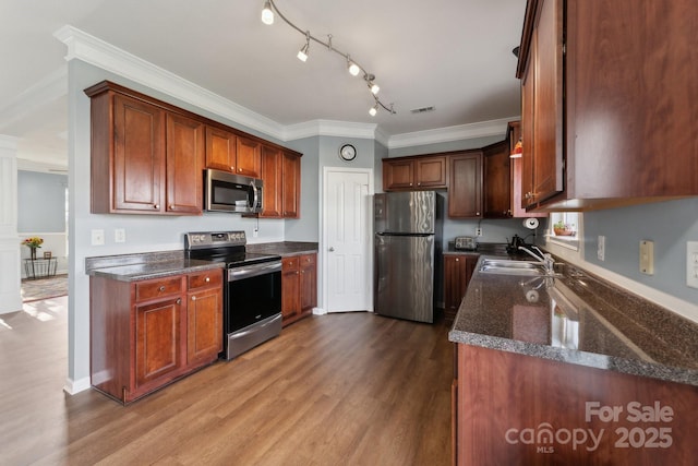 kitchen featuring dark wood-style floors, crown molding, stainless steel appliances, a sink, and dark stone counters