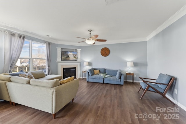 living area featuring baseboards, a glass covered fireplace, dark wood finished floors, and crown molding