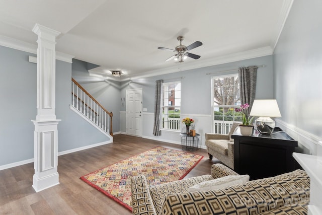 living area featuring wood finished floors, a ceiling fan, stairs, ornamental molding, and decorative columns