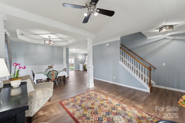 interior space featuring a raised ceiling, wood finished floors, stairs, crown molding, and ornate columns