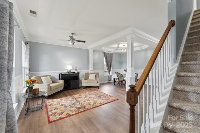 living area with wood finished floors, visible vents, stairs, ornate columns, and crown molding