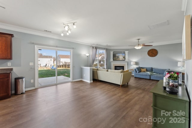 living area featuring visible vents, dark wood finished floors, crown molding, and a glass covered fireplace