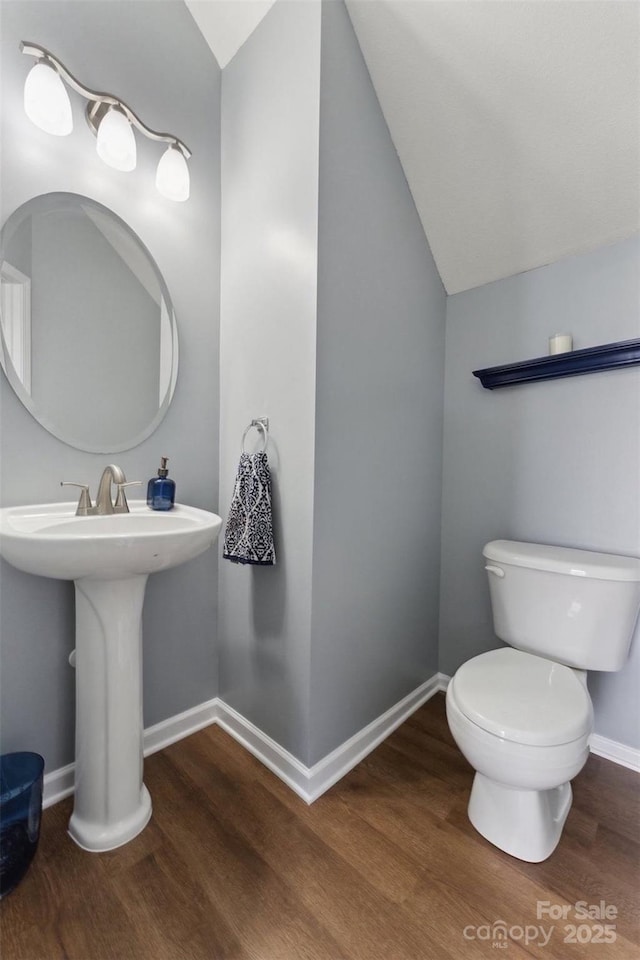 half bath featuring lofted ceiling, baseboards, toilet, and wood finished floors