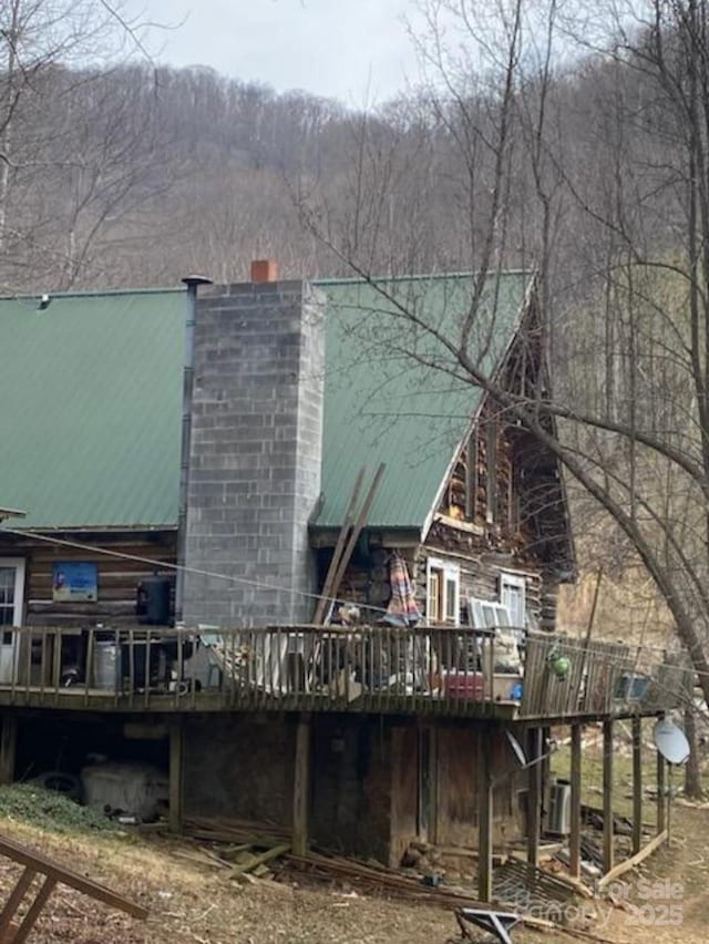 back of house with a chimney, a wooden deck, metal roof, and a view of trees