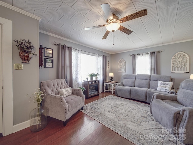 living area featuring baseboards, ceiling fan, dark wood-style flooring, and crown molding