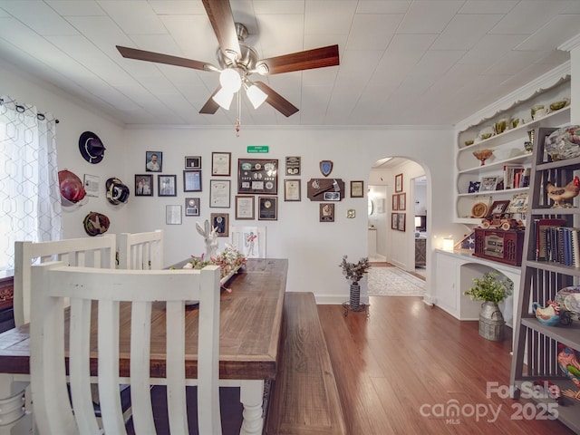 dining space with wood finished floors, arched walkways, ceiling fan, and crown molding
