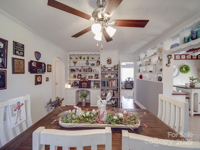 dining space with ceiling fan, arched walkways, built in shelves, and ornamental molding