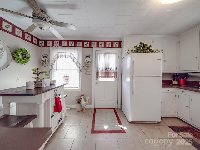 kitchen with a ceiling fan, dark countertops, freestanding refrigerator, light tile patterned flooring, and white cabinets