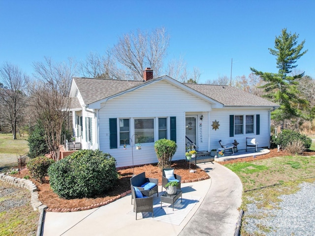 view of front of property with a patio area, a chimney, and a shingled roof