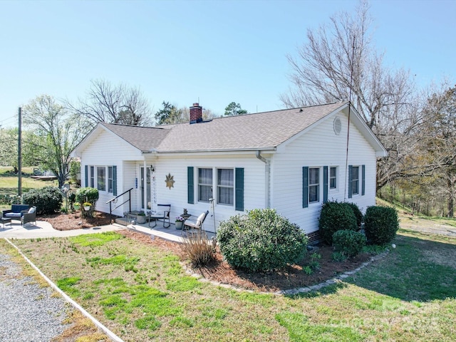 single story home featuring a front yard, roof with shingles, a chimney, entry steps, and a patio area