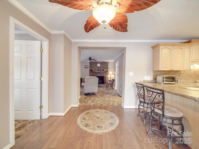 kitchen with a breakfast bar area, light brown cabinets, light wood-type flooring, and ornamental molding