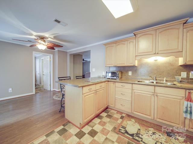 kitchen featuring a sink, a peninsula, visible vents, and light brown cabinetry