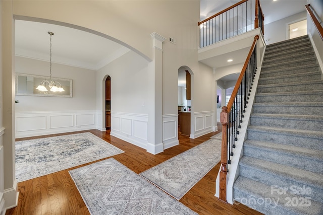 foyer with visible vents, crown molding, stairs, wood finished floors, and a notable chandelier