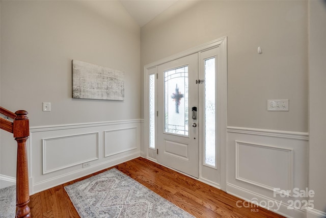 entryway with wood finished floors, wainscoting, and vaulted ceiling