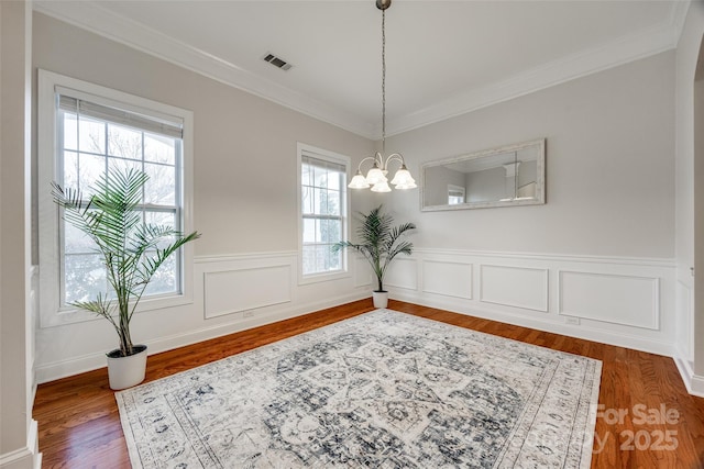 dining room featuring crown molding, a notable chandelier, wood finished floors, and wainscoting