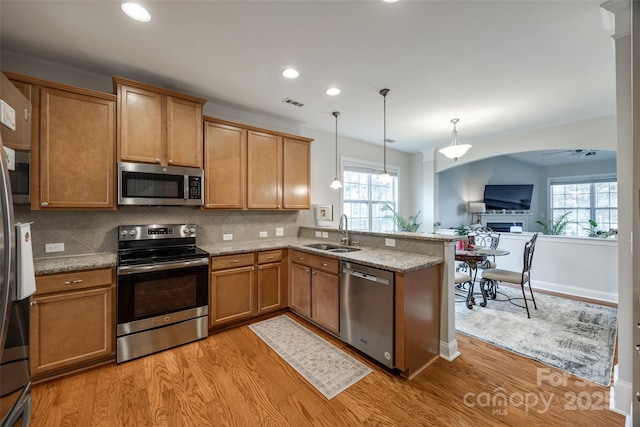 kitchen with a peninsula, a sink, appliances with stainless steel finishes, light wood-type flooring, and backsplash