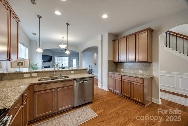 kitchen with brown cabinets, appliances with stainless steel finishes, a peninsula, arched walkways, and a sink