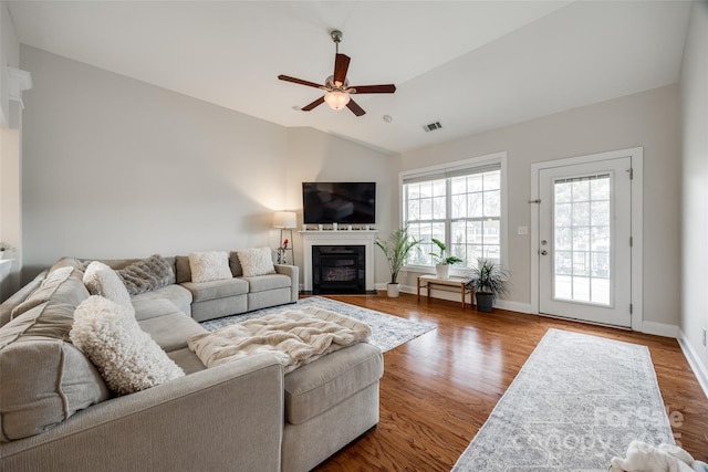 living area with a glass covered fireplace, wood finished floors, visible vents, and vaulted ceiling