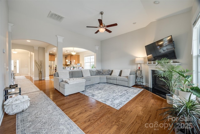 living room with a glass covered fireplace, wood finished floors, arched walkways, and visible vents