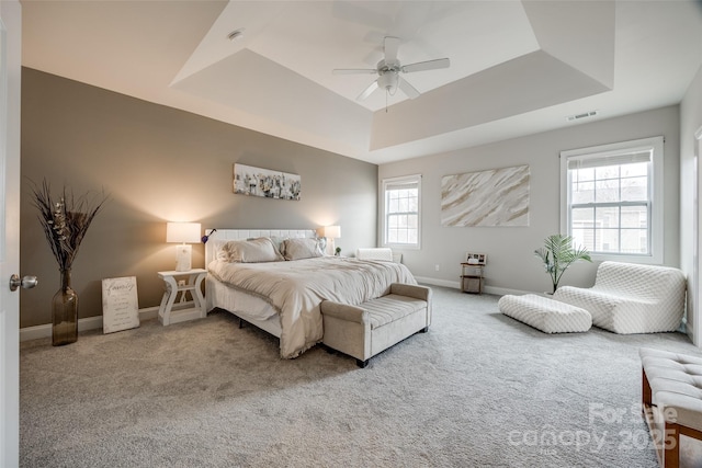 carpeted bedroom with a ceiling fan, a tray ceiling, baseboards, and visible vents