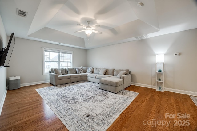 living room with a tray ceiling, visible vents, and wood finished floors