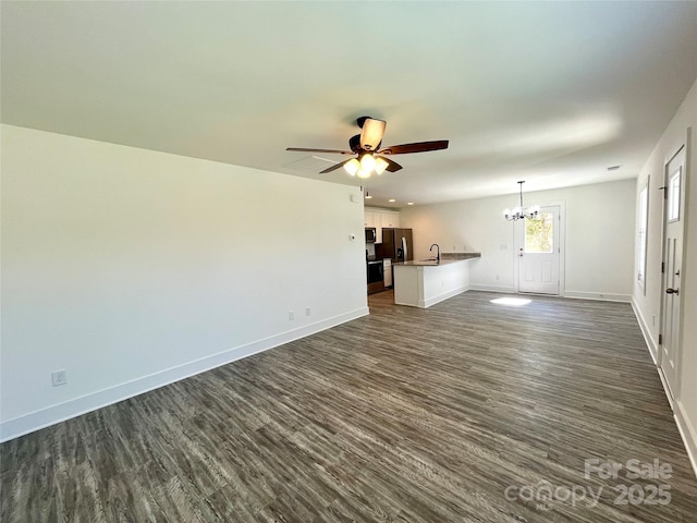 unfurnished living room with dark wood-style floors, ceiling fan with notable chandelier, a sink, and baseboards