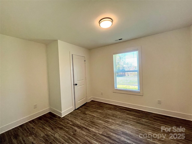 unfurnished room featuring dark wood finished floors, visible vents, and baseboards