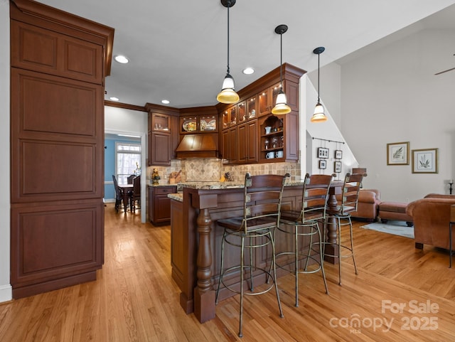 kitchen featuring light wood-style flooring, decorative backsplash, a kitchen breakfast bar, glass insert cabinets, and custom exhaust hood