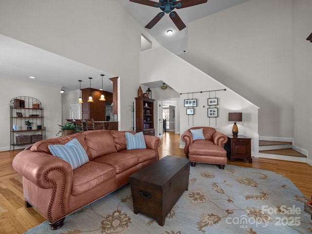 living area featuring a towering ceiling, ceiling fan, baseboards, and wood finished floors