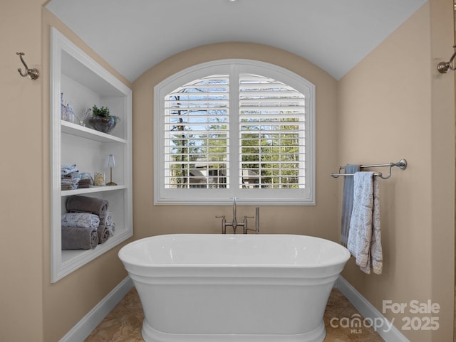 full bathroom with vaulted ceiling, built in shelves, baseboards, and a freestanding bath