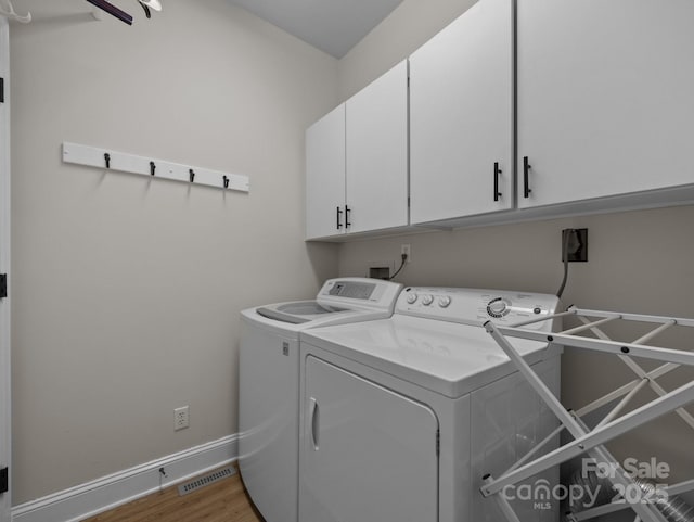 washroom with washing machine and clothes dryer, visible vents, baseboards, wood finished floors, and cabinet space