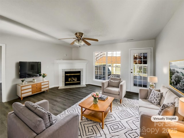 living area with a tile fireplace, ceiling fan, baseboards, and wood finished floors