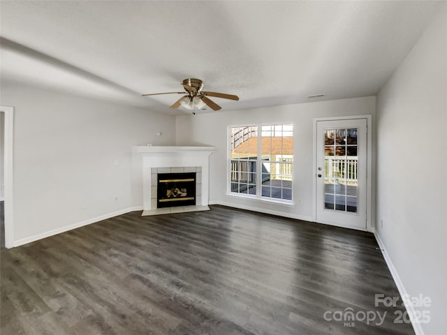 unfurnished living room featuring ceiling fan, baseboards, dark wood finished floors, and a tiled fireplace