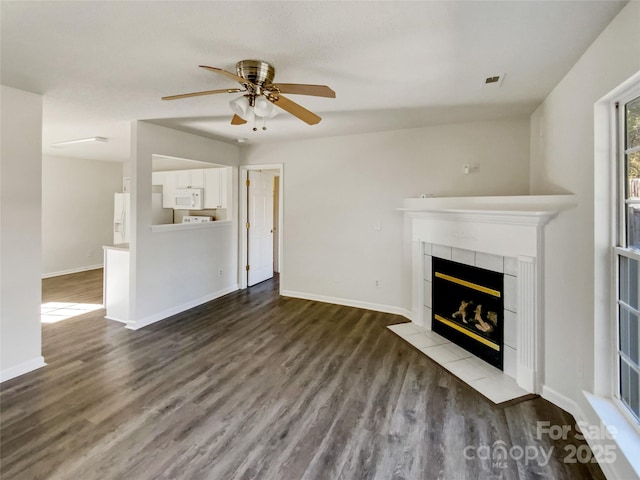 unfurnished living room with baseboards, visible vents, a tiled fireplace, and wood finished floors