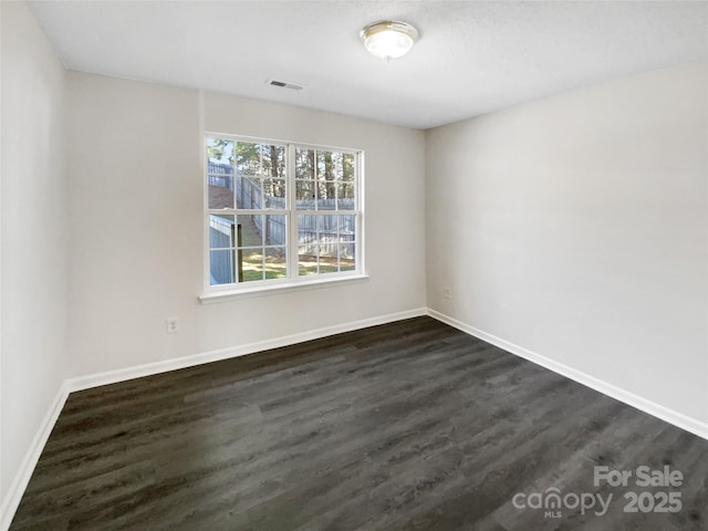 empty room with baseboards, visible vents, and dark wood-style flooring