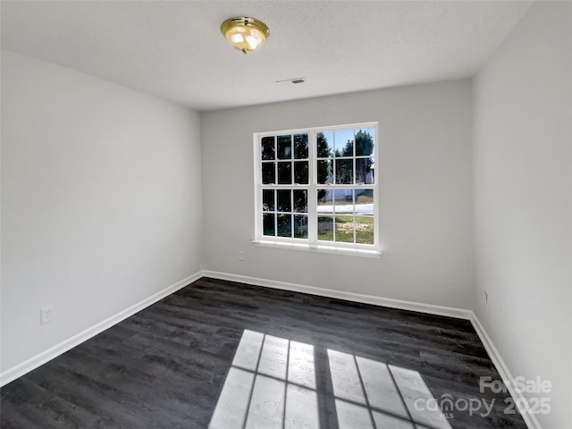 spare room featuring dark wood-style flooring, visible vents, and baseboards