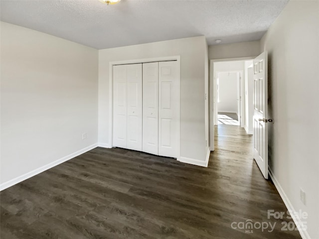 unfurnished bedroom featuring dark wood-type flooring, a textured ceiling, and baseboards