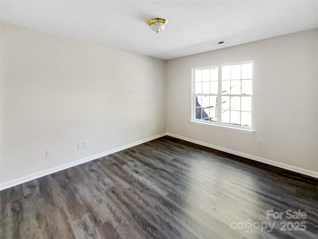 spare room featuring visible vents, baseboards, and dark wood finished floors