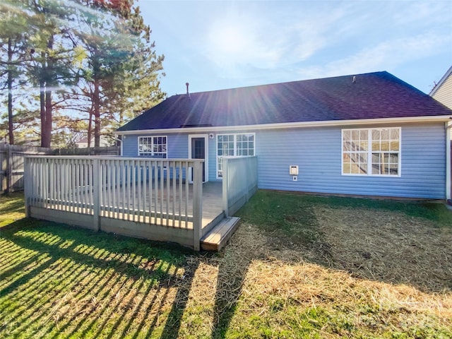 rear view of property with a deck, roof with shingles, a lawn, and fence