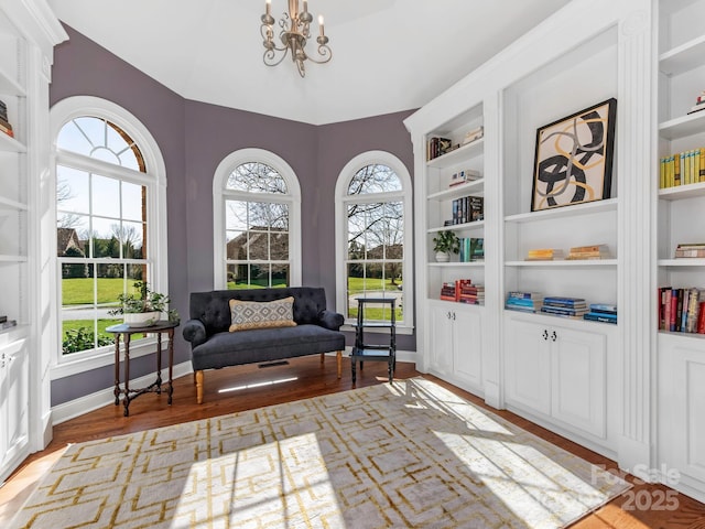 living area with a chandelier, built in features, baseboards, and wood finished floors