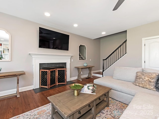 living room with stairs, a fireplace with flush hearth, wood finished floors, and baseboards