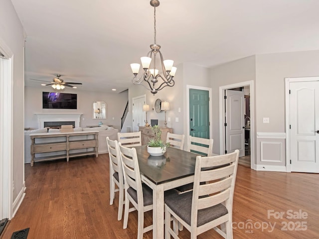 dining area featuring visible vents, ceiling fan with notable chandelier, a fireplace, and dark wood-type flooring