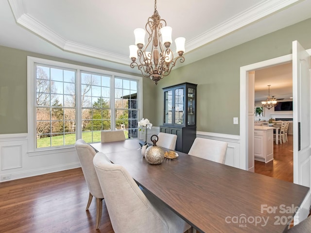 dining space featuring a tray ceiling, a wainscoted wall, a chandelier, and dark wood-style flooring