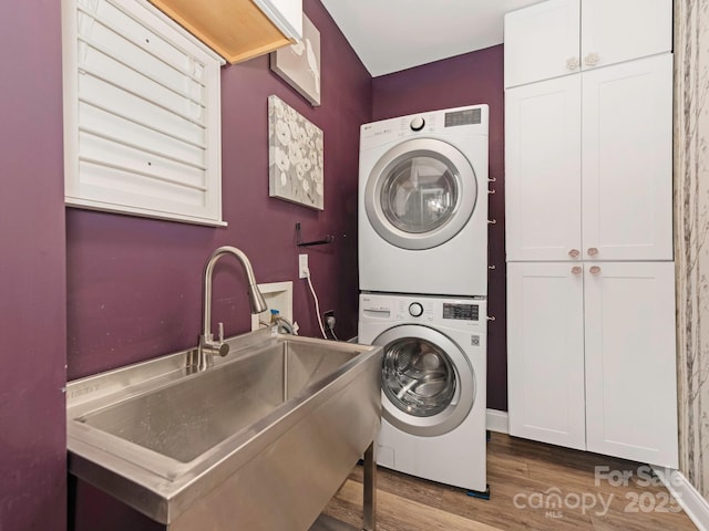 washroom with wood finished floors, cabinet space, stacked washer / drying machine, and a sink